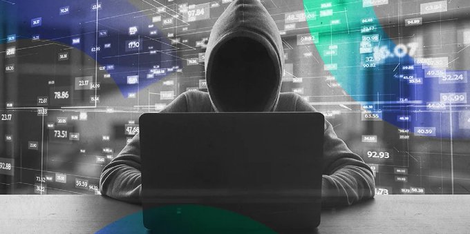 A hooded figure sits at a laptop against a backdrop of stock tickers and financial data, symbolizing an anonymous cryptocurrency scammer. The image visually reinforces the post's warning about a sophisticated phishing scheme that impersonated Flare Network's staking website to steal 8.5 million USD in XRP through fake FXRP platforms and fabricated media content.