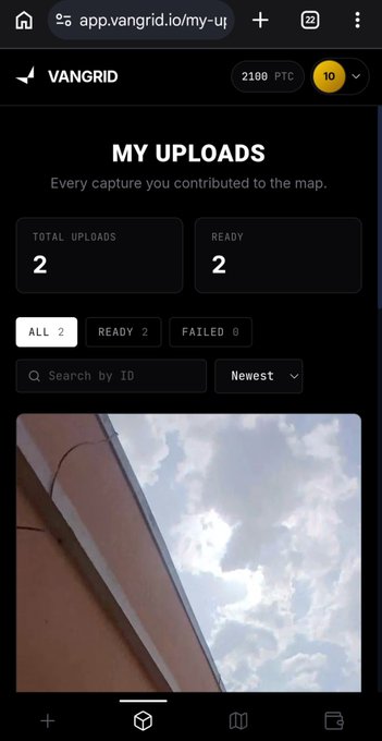 A screenshot of the VANGRID app's "MY UPLOADS" dashboard showing 2 total and 2 ready contributions, with a preview image of a building against a cloudy sky—illustrating how the platform collects real-world captures to provide Physical AI with genuine observational data rather than simulated environments.