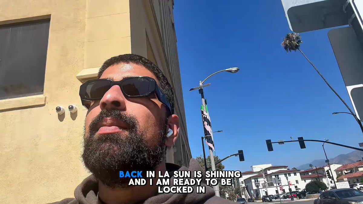 The image features a man wearing sunglasses, standing outside with his back facing the camera. The background shows an urban setting with buildings and traffic lights. There are also several cars parked nearby. The caption of the image reads "Back in LA sun is shining and I am ready to be locked in", which seems to be related to the post about a World Cup challenge or a similar event.