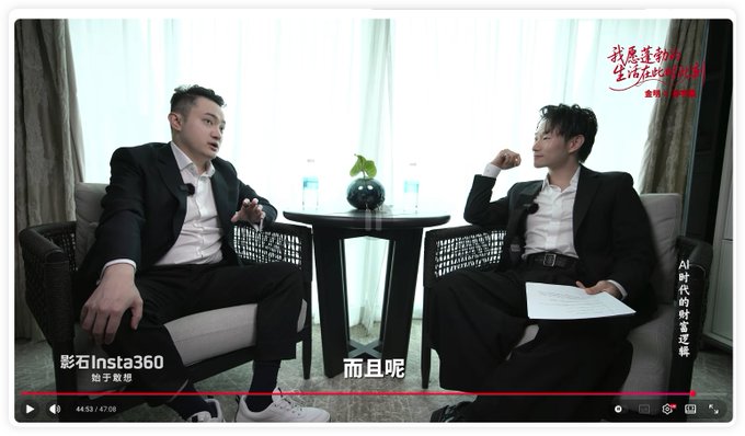 The image captures a video interview moment showing two men in suits seated across from each other at a table, with Justin Sun on the left and an interviewer on the right holding notes. The scene is from a video titled "AI时代的财富密码" (Wealth Code of the AI Era) at 44:53/47:08, where the visible subtitle "而且呢" suggests a continuation of the discussion about Tron's transaction fees that the accompanying post describes.