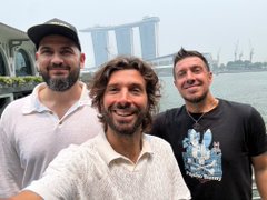 Three men pose for a selfie in front of the Marina Bay Sands hotel in Singapore.