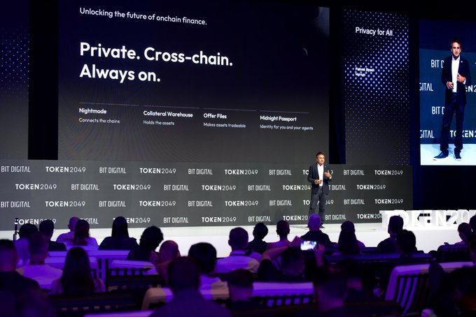 A presenter speaks on stage at TOKEN2049 BIT DIGITAL beneath a large screen highlighting Midnight's key features—"Nightmode," "Collateral Warehouse," "Offer Files," and "Midnight Passport"—under the tagline "Private. Cross-chain. Always on." The keynote illustrates the company's vision of serving as the privacy layer for every blockchain, introducing tools like the Midnight Passport to unify user identity across chains.