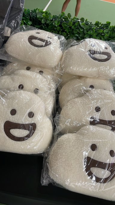 A photo of several plush smiley-face toys with white fuzzy bodies and brown embroidered faces, individually wrapped in clear plastic bags and arranged in a display.