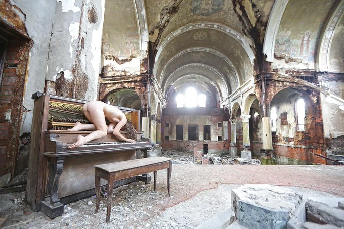 A nude figure is embracing a decaying piano within a ruined church in this photographic portrait, titled "Salvation Will Never Come 1/1" and available on @objktcom.
