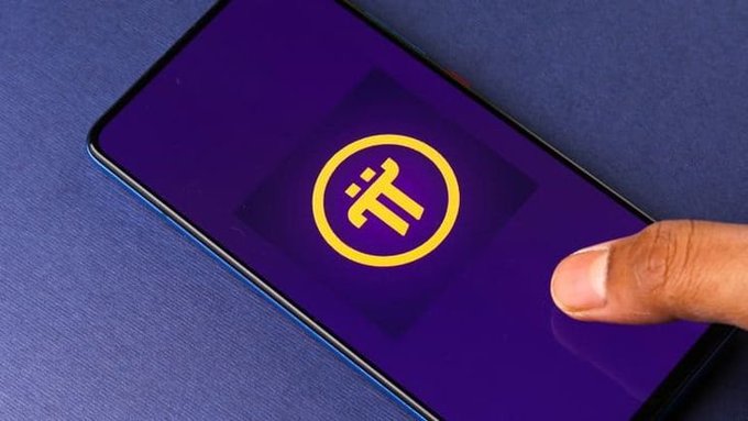 A hand holding a smartphone displaying a yellow Pi (Pi Network) cryptocurrency logo on a purple background.