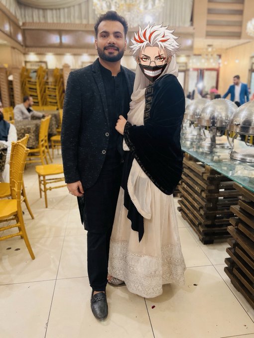 A photo of a man in a black suit posing with a person dressed in a white and black costume with an anime-style mask (resembling Kaneki from Tokyo Ghoul) at what appears to be an upscale restaurant or banquet hall.