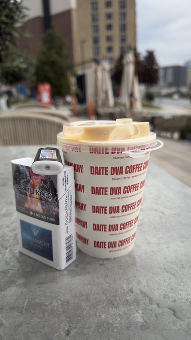 A pack of Davidoff "Gold" cigarettes sits next to a large cup from Daite DVA Coffee Co. on an outdoor metal table.