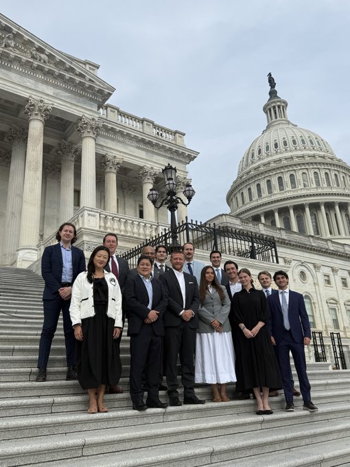 A group of approximately twelve people in business attire pose together on the steps of the U.S. Capitol building.