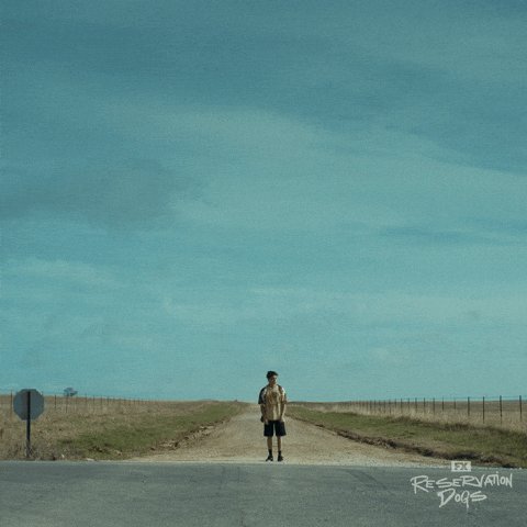 The image features a man standing alone on an empty road, with no other people or vehicles visible around him. The scene appears to be set in a rural area, as there are no signs of urban life such as buildings or traffic. The caption related to this image reads "What happened? Are we back in Ghost Town? Where'e you all at $XRP fam?". This suggests that the man might have been involved in an event or gathering where people were paid to take pictures, and he is now standing alone on a road with his picture taken.