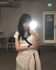 A young woman with long dark hair takes a mirror selfie in what appears to be a public building, with the camera flash visible.