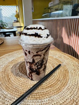A chocolate frappuccino topped with whipped cream and chocolate drizzle sits on a woven placemat in a bright café. While the image showcases a tasty beverage, it has no direct connection to the Solana wallet comment request.