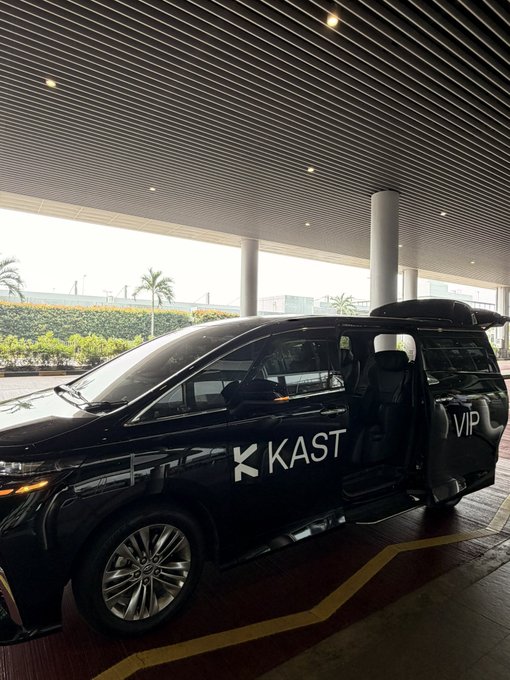 A black VIP van with 'KAST' branding is parked with its door open at a covered terminal or airport pickup area.