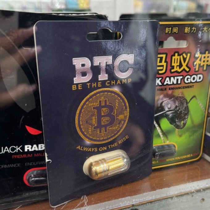 A novelty product display showing a blister pack of 'BTC BE THE CHAMP - ALWAYS ON THE RISE' pills with a Bitcoin logo, displayed next to other questionable male enhancement products including 'JACK RABBIT' and 'K ANT GOD' with Chinese text.