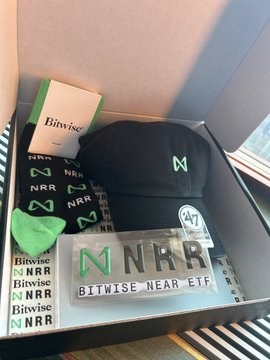 A promotional gift box from Bitwise celebrating the upcoming Bitwise NEAR ETF (ticker: NRR) is displayed, containing branded swag including a black cap, stickers, a card, and a "NRR Bitwise NEAR ETF" plaque—all marked with the green "M" logo.