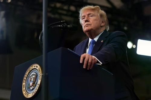 President Donald Trump stands at a podium bearing the Presidential Seal, looking upward during a speech.