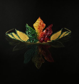 The image features a crown made of leaves, with each leaf having a different color - yellow, green, red, and orange. The crown appears to be a work of art or a decorative piece, possibly used for a special occasion or celebration. The colors of the leaves are vibrant and eye-catching, making it an interesting focal point in the image.
