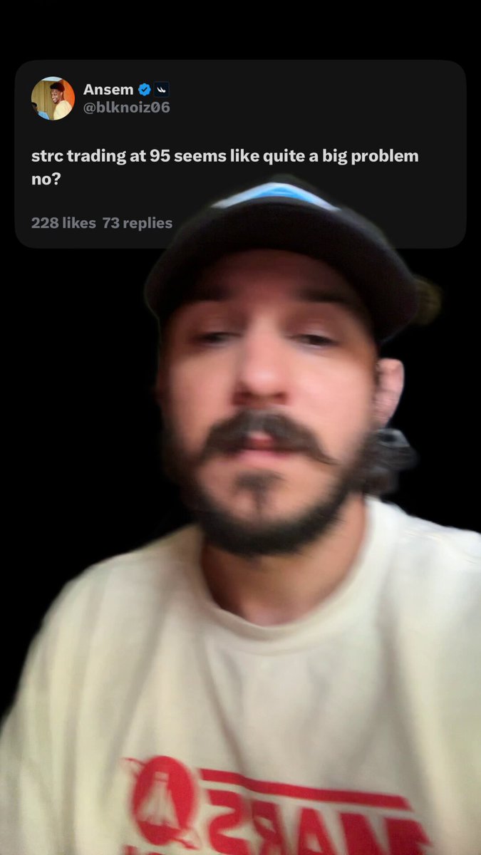 The image features a man wearing a white shirt with red text, which says "QR" at the bottom of his shirt. The man has a beard and mustache, giving him a distinctive look. He appears to be making a face or showing off his facial hair for the camera. The post he is interacting with seems to be about trading Bitcoin, as it contains a question asking if trading is like a big problem.