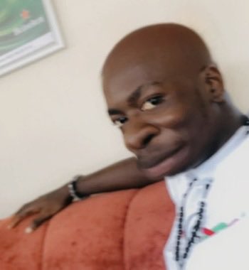 A man takes a selfie while sitting on an orange couch, with a framed picture partially visible in the background. His skeptical, side-eye expression aligns well with the post's dismissive tone toward someone wanting to launch a token without experience minting NFTs.