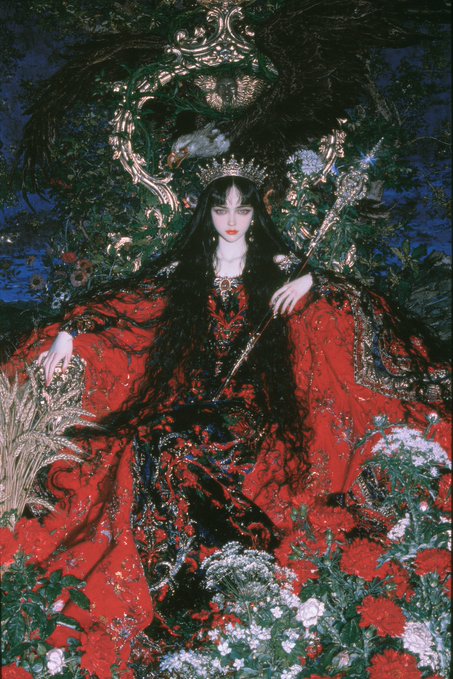 A dark, ornate fantasy illustration of a pale-skinned queen in an elaborate red and black gown, wearing a crown and holding a scepter, surrounded by lush flowers and foliage.