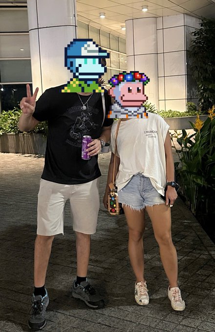 A photo of a couple posing outdoors at night, with their faces obscured by pixel art of a blue-haired anime character and a colorful monkey character; the person on the left wears a black t-shirt and white shorts holding a purple can, while the person on the right wears a white shirt and denim shorts.