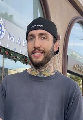 A man with a backwards "Member angel" cap, facial tattoos, and a gray t-shirt smiles at the camera outside a storefront. The image likely depicts FaZe Banks, a co-founder of the FaZe Clan esports organization, in connection with the post highlighting his bullish commentary on the $CATE cryptocurrency.