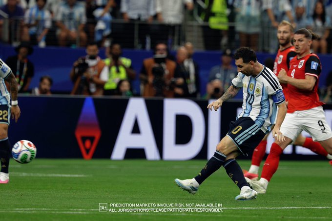 A soccer player wearing an Argentina jersey (#10) is captured mid-kick during what appears to be a match, with opposing players in red and white jerseys and a crowd visible in the background. A banner reading "ADIDAS" and a small disclaimer about prediction markets ("PREDICTION MARKETS INVOLVE RISK. NOT AVAILABLE IN ALL JURISDICTIONS. PLEASE PARTICIPATE RESPONSIBLY.") appear in the image, with the disclaimer tying into the post's mention of Robinhood's prediction market on its new blockchain.