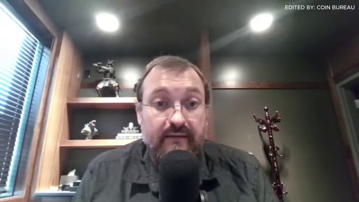 The image shows a man wearing glasses sitting at a desk with a microphone in front of him. He appears to be talking into the microphone, possibly discussing the concept of "Cardano" or sharing his thoughts about a failed project named "ADA." The man is dressed in a black shirt and has a beard.