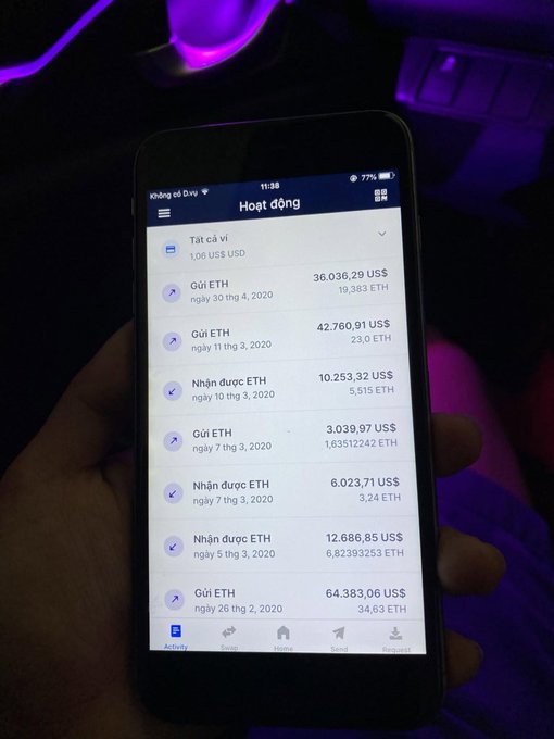 A photograph of a smartphone displaying a crypto wallet activity page in Vietnamese ("Hoạt động"), listing recent ETH sends and receives with USD values, held by a hand in a room with purple lighting.