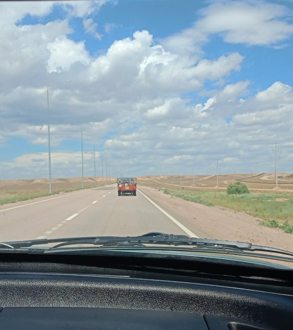 A view from inside a car driving on a highway, with a red utility vehicle ahead and dramatic clouds filling the blue sky.