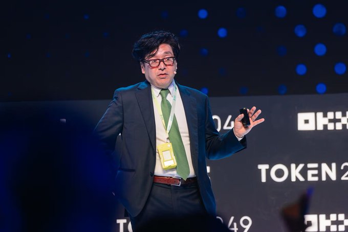 Tom Lee, who helped found BitMine Immersion Technologies, gestures while speaking at a conference, with "TOKEN2049" visible on the backdrop. The image relates to BitMine's recent acquisition of 27,801 ETH over the past week, highlighted in the accompanying post.
