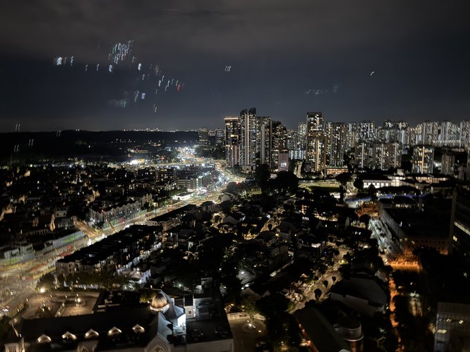 An aerial nighttime view of a city skyline with illuminated high-rise buildings and a bustling street below.