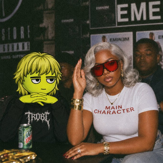 A photo featuring an anime character with green skin and blonde hair next to a real person wearing red sunglasses and a white t-shirt that reads "MAIN CHARACTER."