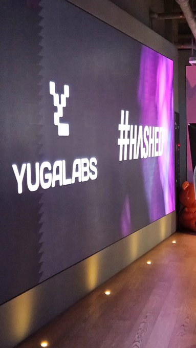 Illuminated signage reading 'YUGALABS' and '#THASHED' on a dark wall with purple lighting accents.