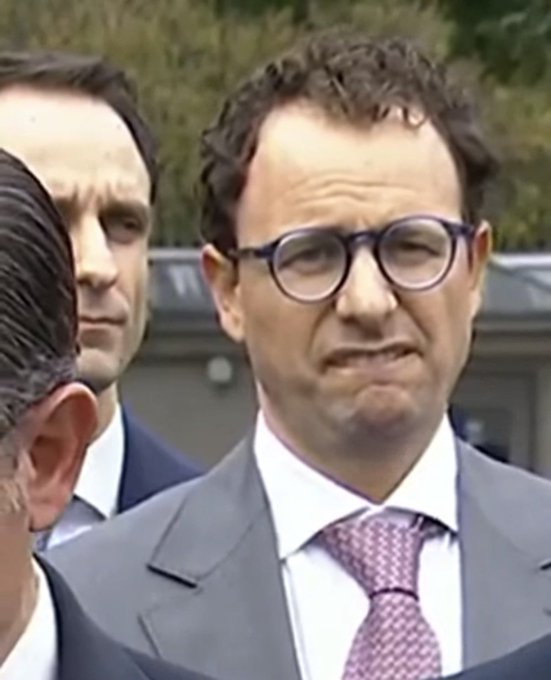 Captures a man in a dark suit and tie, looking off-camera with a serious expression.