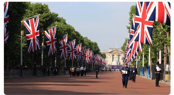 Union Jack flags line a ceremonial London street, likely The Mall leading to Buckingham Palace, with police officers standing watch. The image symbolizes Robinhood's official launch in the United Kingdom, with the British flags representing its new UK market entry.