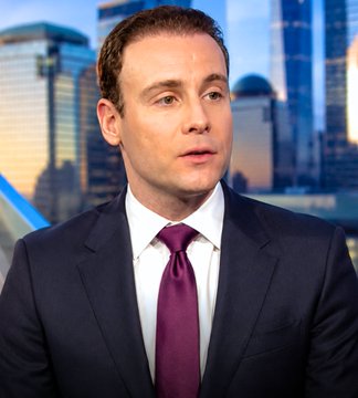 A man in a dark suit with a maroon tie and white shirt is shown speaking, likely during a broadcast or interview, with a city skyline visible in the background. The image accompanies a post about the CFTC Chairman's remarks on the Bitcoin and Crypto Clarity Act being close to passing but facing political obstacles.