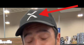 The image features a man with brown hair wearing a black baseball cap that has a white "X" on it. The caption of the image reads "@RayFuentesIO does an awesome Best Buy / Tangem @Tangem wallet, 13 minute video". The man is looking directly at the camera and appears to be in a store or a similar setting.