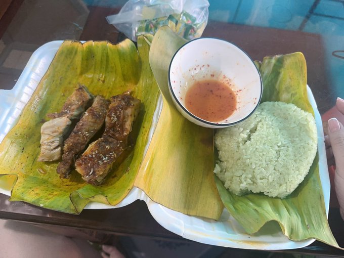 A plate of food served on banana leaves, featuring grilled meat, sticky rice, and a small bowl of dipping sauce.