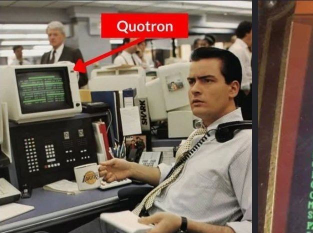 A still from the movie Wall Street showing Charlie Sheen sitting at a desk on the phone, with a red arrow label 'Quotron' pointing to the stock terminal screen.