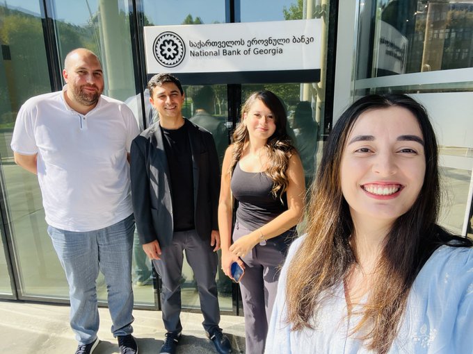 A group of four people smile for a selfie outside the National Bank of Georgia, whose name is displayed in both Georgian and English on the building's signage. The image illustrates the visit mentioned in the post, where the team met with Georgia's central bank to discuss Solana's global work and stablecoins.