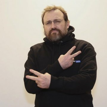 A bearded man in glasses and a black hoodie making hand gestures. The post suggests this is Charles Hoskinson, the Cardano founder, pictured during a talk where he warned of a "quantum apocalypse" that could threaten Bitcoin's dormant coins and governance model.