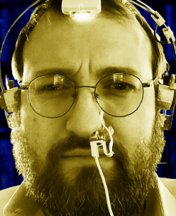 A close-up sepia-toned portrait shows a bearded man wearing glasses and a complex head-mounted device with a wire across his face.