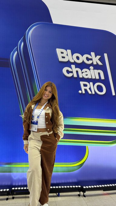 A woman smiling at the camera while standing in front of a 'Blockchain Rio' sign at an event.