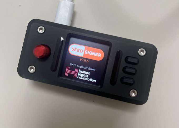 A black SeedSigner device (v0.8.6) displays its boot screen acknowledging support from the Human Rights Foundation, featuring a red button and three side controls, with a white antenna protruding from the top. The image directly illustrates the post's endorsement of SeedSigner, a DIY Bitcoin hardware wallet built around a Teensy microcontroller, showing the device in its powered-on, ready-to-use state.