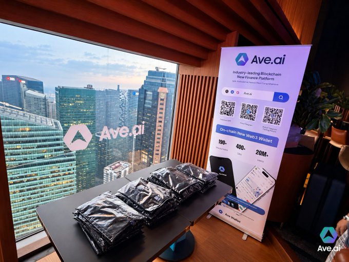 An indoor setting with a view of a city skyline, featuring an 'Ave.ai' branded banner promoting an 'On-chain New Web 3 Wallet' with QR codes, and black merchandise bags on a table.