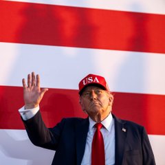 President Trump, wearing a red "USA" cap, waves in front of an American flag backdrop. The image accompanies news of his planned attendance at a White House meeting with crypto and prediction market executives, joined by CFTC Chair Michael Selig and SEC Chair Paul Atkins.
