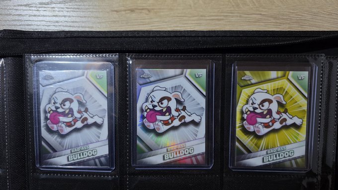 A collector's binder displaying three 'BADASS BULLDOG' trading cards in protective sleeves, featuring a cartoon bulldog with different colored backgrounds.