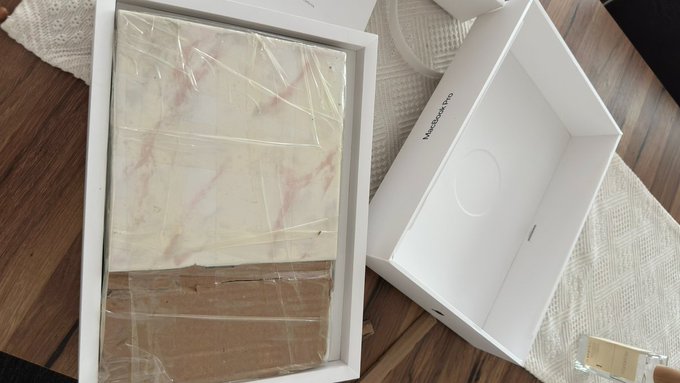 A man receives his MacBook Pro in an Apple box alongside a marble-patterned stone, illustrating the joke about men only reacting when their expensive tech orders come with absurd extras like marble.