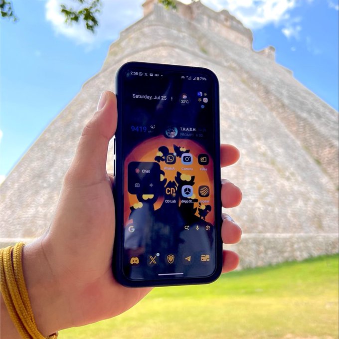 A hand holds up a smartphone displaying a home screen with various app icons (Chat, Search, Camera, Files, CD Lab, App info, Recorder) and a weather widget showing 'Saturday, Jul 25, 30°C', set against the backdrop of a large stone pyramid under a blue sky.