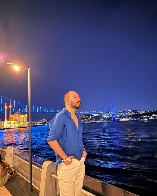 A man stands on a balcony overlooking a city skyline illuminated at night, with a bridge and a mosque visible. This image likely represents a celebratory moment as he marks "Level 30 unlocked" and 8 years in crypto since 2018.